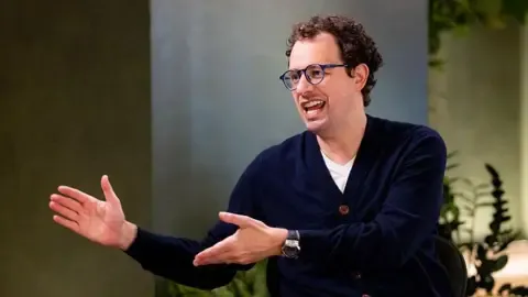 Anthropic CEO Dario Amodei 在采访中发言，背景为植物装饰的会议室